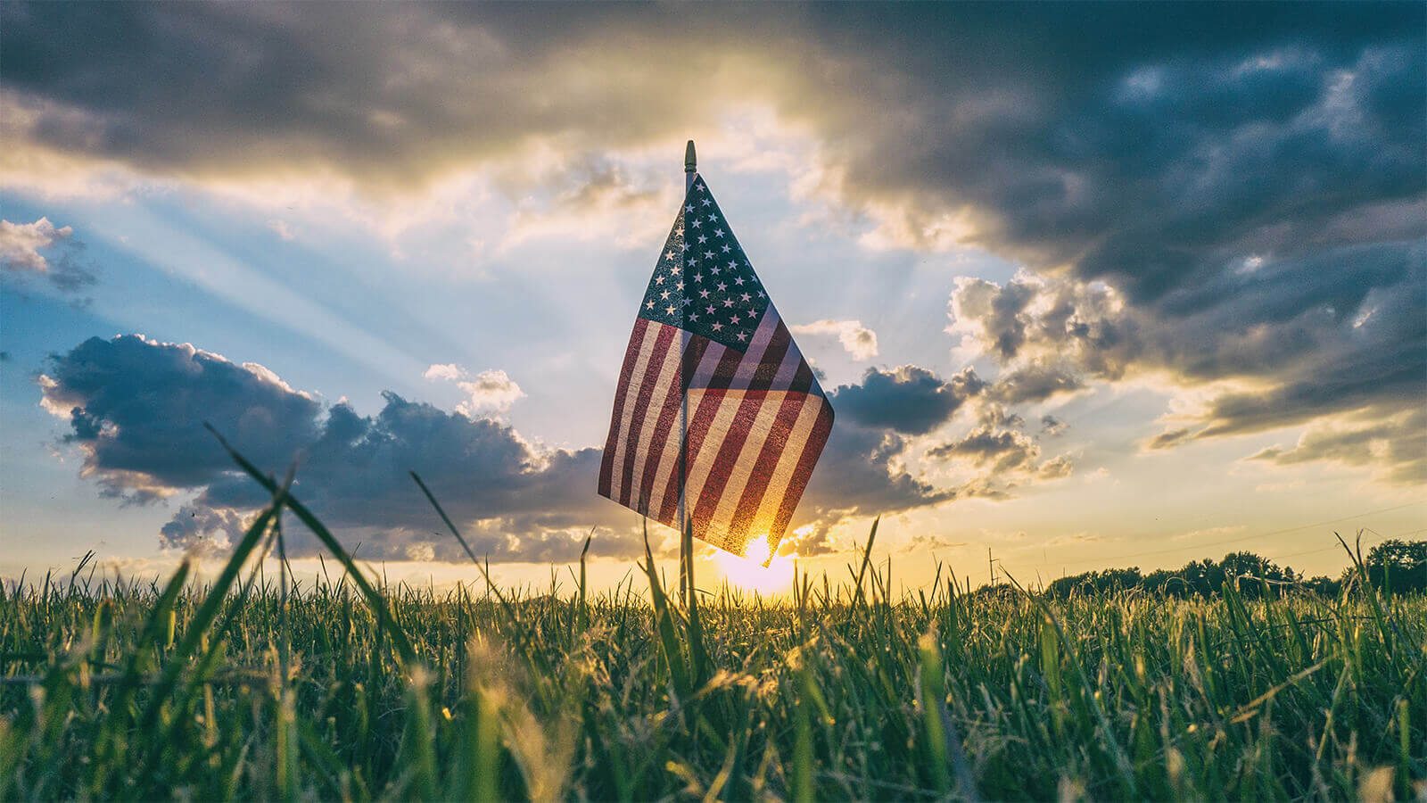 Phootgraph of a US flag in a field with a sunset in the background